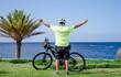 © luciano - Senior man with a bicycle by the ocean, arms outstretched, expressing joy and satisfaction, embracing an active lifestyle, health, and well-being in retirement