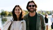 © Bussakon - A man and woman smile together outdoors near water on a sunny day wearing casual jackets and sunglasses