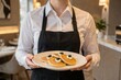 © Julia - Woman in white shirt, black apron, holding plate of Blini with Caviar in modern kitchen. Concept of culinary elegance, featuring thin pancakes with caviar sour cream.