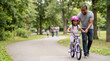 © Xenia - Black father teaching his young daughter to ride a bicycle in the park. Smiling African American dad helping child balance on a purple bike. Family outdoor recreation