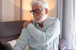 © luciano - Senior man experiencing severe shoulder pain, rubbing his arm and expressing discomfort, dealing with muscle ache, arthritis, injury, and elderly health issues at home