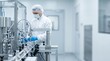 © Eve - Pharmaceutical factory worker in sterile protective uniform operating automated production line conveyor belt with medical vials, medicine manufacturing and biotechnology laboratory concept