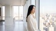 © AspctStyle - Asian business woman looking out window of luxury high-rise apartment at urban city skyline for real estate and financial growth themes