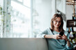 © Westend61 - Smiling woman text messaging through smart phone sitting in cafe