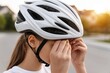© whitestorm - Young woman fastening the chin strap of her white bicycle helmet for safety outdoors.