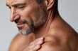 © whitestorm - Close-up portrait of a mature man with a salt and pepper beard, looking down with a thoughtful expression, touching his shoulder.