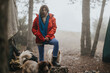 © qunica.com - A woman in a red jacket stands at a foggy mountain campsite with two dogs. Friends share a quiet, misty outdoor moment at their campsite.