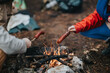 © qunica.com - Two people roast sausages over a small campfire in the woods. A cozy outdoor camping scene with food cooked on sticks.