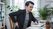 © Febi - Man experiencing back pain while sitting at a desk in a home office, touching his lower back and grimacing in discomfort, surrounded by plants and work documents
