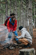 © qunica.com - A group of friends tending a small campfire in a pine forest while preparing for a campsite. The outdoor scene shows companions in warm jackets camping together near mountain trails.