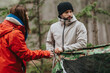 © qunica.com - Two friends set up a camouflage tent in a mountain forest while wearing winter jackets. The pair work together outdoors preparing a campsite in a chilly, wooded landscape.