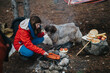 © qunica.com - A woman crouches by a campfire cooking hot dogs while her dog looks on. Casual outdoor camping scene with simple meal preparation and a pet by the fire.