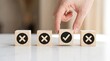 © Iwan - Hand choosing wooden block with checkmark icon among blocks with cross icons on white table