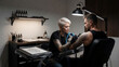© Ano - Eine erfahrene Tätowiererin erstellt in einem stilvollen Tattoo-Studio ein geometrisches Tattoo auf der Schulter eines Kunden. KI Generiert