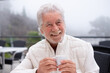 © luciano - Senior man smiling and holding a coffee cup, enjoying a peaceful moment outdoors during foggy weather, celebrating retirement and a relaxed lifestyle