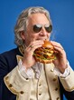 © Robi - Man in historical attire eating large gourmet burger indoors closely