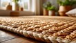 © Asawin - A close-up view of a woven rug with a detailed texture. The rug is made of natural fibers and lies on a wooden floor, with potted plants blurred in the background