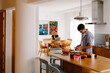 © Adrian Rodd/Stocksy - A man prepares food while a blonde woman works on her laptop behind.