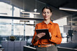 © Stock 4 You - Young latin or indian businesswoman using digital tablet standing in modern office. Confident professional woman checking data, browsing online application in corporate workplace, business technology.