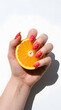 © Suratama - Woman hand with colorful chevron nail art holding a fresh orange slice on white background.