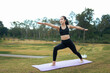 © PaeGAG - Young woman practicing yoga warrior pose outdoors in park
