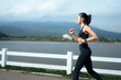 © PaeGAG - Young woman running outdoors by lake exercising for fitness