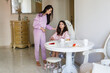 © millaf (Nemchinova) - Pretty little girl in pink pajamas with her mom eating in kitchen