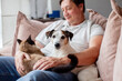 © Tatyana Gladskih - Man sitting on a sofa and hugging his dog and cat. Owner relaxing at home with domestic pets. Friendship between human and animal, pet care, cozy lifestyle and companionship concept.