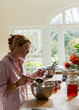 © Marc Romanelli - young woman in light filled kitchen using mixing bowl and cooking