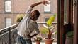© Ahsan - A young man stretches on a plant-filled city balcony in morning light, perfect for wellness, home fitness, urban lifestyle, or self-care campaigns.