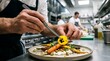 © Kesy Visual Studio - Close up of a professional male chef hands using tweezers to place an edible yellow flower garnish on a gourmet roasted carrot dish.