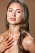© SergeiPh - A beautiful girl poses against a brown background wearing a white strapless dress. Her long, wavy hair gently frames her shoulders.