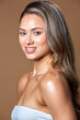 © SergeiPh - A beautiful girl poses against a brown background wearing a white strapless dress. Her long, wavy hair gently frames her shoulders.
