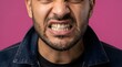 © Yassine - Close up portrait of a bearded man clenching his teeth in anger against a vivid solid pink studio background wall