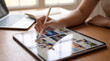 © Watercolor_Kawaii - Graphic designer editing image layout on tablet with stylus at desk near laptop