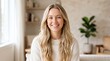 © Karan - Portrait of a happy young woman with long wavy blonde hair smiling at the camera in a bright home interior setting