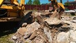 © MIKHAIL - Excavator bucket digging into a pile of broken concrete, rebar, and rubble during demolition work on a construction site under a clear blue sky, showing urban renewal activity