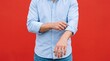 © Shiv - Man wearing light blue button down shirt rolling up sleeves standing against solid red background with clothing