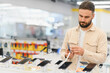 © Serhii - Customer choosing smartphone in electronics store, examining new mobile phone