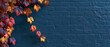 © Olga Ко - Fond d'automne : feuilles colorées sur un mur de briques bleu foncé avec espace de copie.