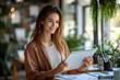 © Milana - Young woman in a plant-filled modern workspace holding a tablet over paperwork at a desk, appearing focused and calm in warm natural light