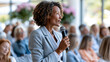 © Nataliya - Faceless confident Black woman speaking at indoor gender equality event with engaged audience, diversity advocacy concept, social event photography, blurred event background, with