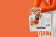 © Pixel-Shot - Woman in orange blazer with gold jewelry holding a fashion magazine on a white chair against an orange background, the magazine features images of models and text, resting on a white chair
