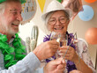 © luciano - Senior couple toasting champagne and sparklers, celebrating a birthday, happy and enjoying a festive party atmosphere, wearing hats and leis, smiling