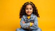 © Goreng - Young girl with curly hair smiles with arms crossed, wearing denim jacket on a yellow backdrop