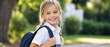 © Vasiliy - Portrait of smiling young girl with backpack outdoors. Happy blonde student in school uniform against blurred green background. Back to school concept