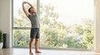 © Xenia - Smiling man stretching his arms upwards in front of a large window. Adult male doing a morning flexibility routine at home. Healthy and active lifestyle