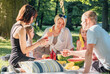 © Soloviova Liudmyla - Happy family and friends having relaxing picnic in sunny summer lush park sitting on cozy blanket on grass eating fresh sweet watermelon and yellow corn enjoying outdoor weekend leisure time together