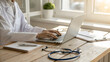 © Rimpa - Doctor typing on a laptop computer at a desk with a stethoscope and medical chart in an office