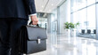 © nuruddean - Businessman holding briefcase in modern office corridor.